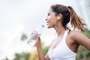 Athletic woman hydrating drinking water during summer