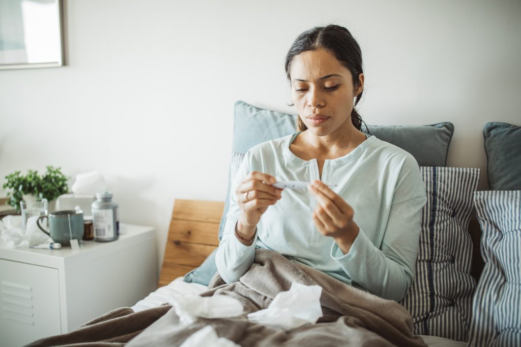 Woman with flu in bed, she use thermometer to measure temperature