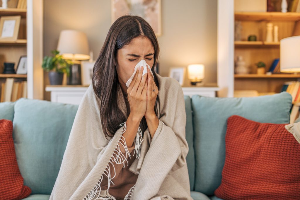 A young woman lying on the sofa in the living room, feeling sick with respiratory illness.